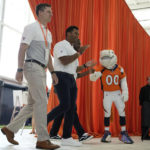 
              From left to right, Denver Broncos quarterbacks Brett Rypien, Russell Wilson and Josh Johnson are greeted by mascot Miles (00) while being introduced at the NFL football team's kickoff luncheon Friday, Aug. 26, 2022, at the Broncos' headquarters in Centennial, Colo. (AP Photo/David Zalubowski)
            