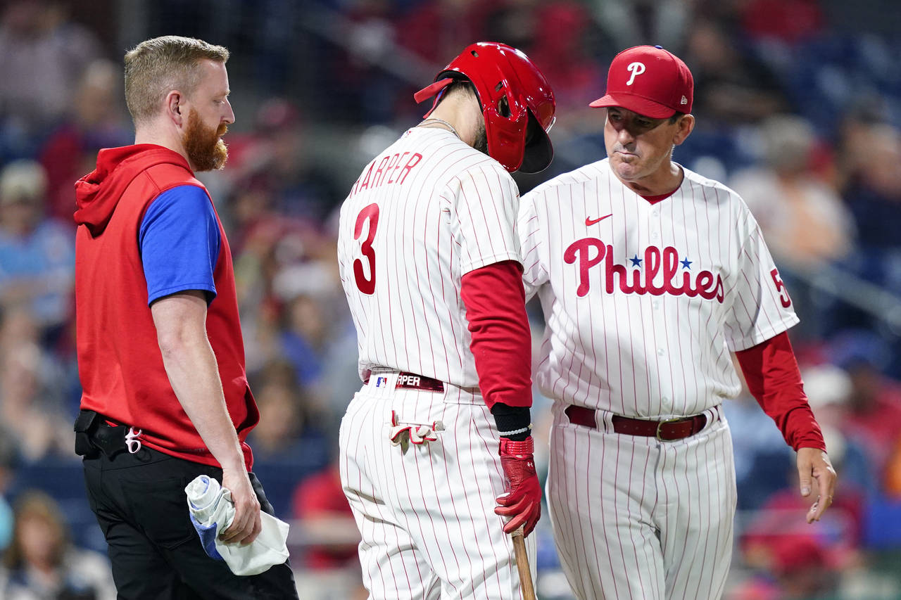 Philadelphia Phillies' Bryce Harper, center, is checked on by interim manager Rob Thomson, right, d...