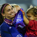 
              United States' Alex Morgan, left, holds her daughter Charlie Elena Carrasco as she listens to Cindy Parlow Cone, president of the U.S. Soccer Federation, speak during an event with the federation, U.S. Women's National Team Players Association and the U.S. National Soccer Team Players Association signing new collective bargaining agreements following the women's match against Nigeria at Audi Field, Tuesday, Sept. 6, 2022, in Washington. The U.S. won 2-1. (AP Photo/Julio Cortez)
            