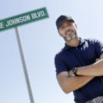 
              FILE - Driver Jimmie Johnson poses in front of a street sign after the street was named for him outside Kentucky Speedway before a NASCAR Cup Series auto race Sunday, July 12, 2020, in Sparta, Ky.  The Seven-time NASCAR champion is retiring from full-time racing and will turn his focus toward spending time with family. He figures his future schedule will include no more than 10 bucket list events and has his sights set on the 24 Hours of Le Mans. (AP Photo/Mark Humphrey, File)
            