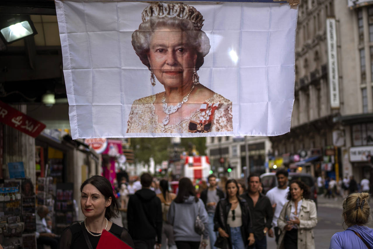 People walk past a flag with a portrait of Queen Elizabeth II in central London, Monday, Sept. 12, ...