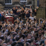 
              People attend the procession of Queen Elizabeth II's coffin, from the Palace of Holyroodhouse to St Giles Cathedral, on the Royal Mile in Edinburgh, Scotland, Monday Sept. 12, 2022. Britain's longest-reigning monarch who was a rock of stability across much of a turbulent century, died Thursday Sept. 8, 2022, after 70 years on the throne. She was 96. (AP Photo/Bernat Armangue)
            