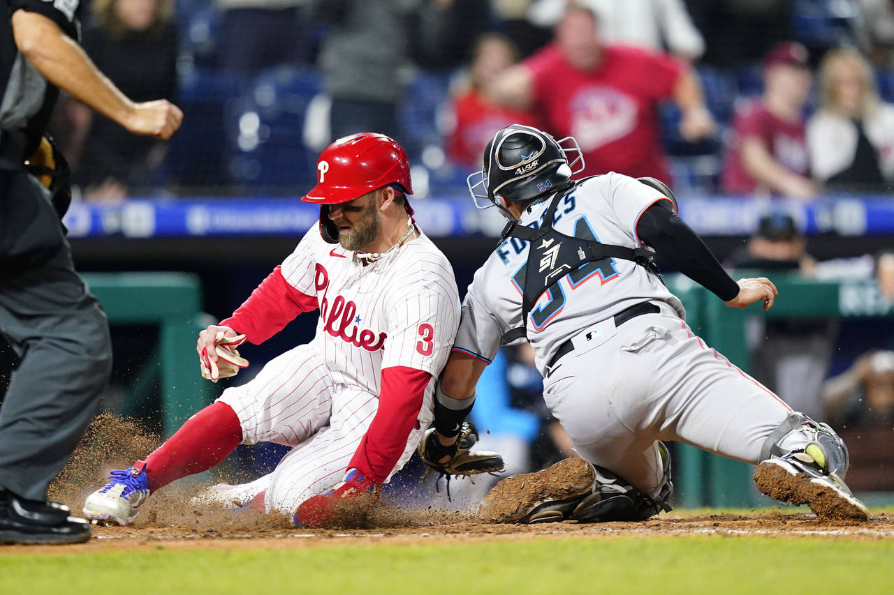 Philadelphia Phillies' Bryce Harper, left, scores the game-winning run past Miami Marlins catcher N...