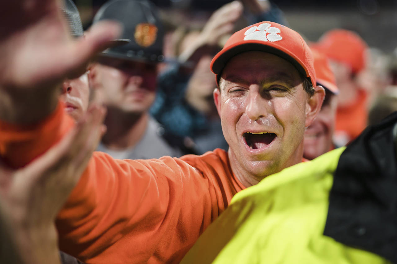 Clemson head coach Dabo Swinney celebrates with fans as he walks off the field after defeating Nort...