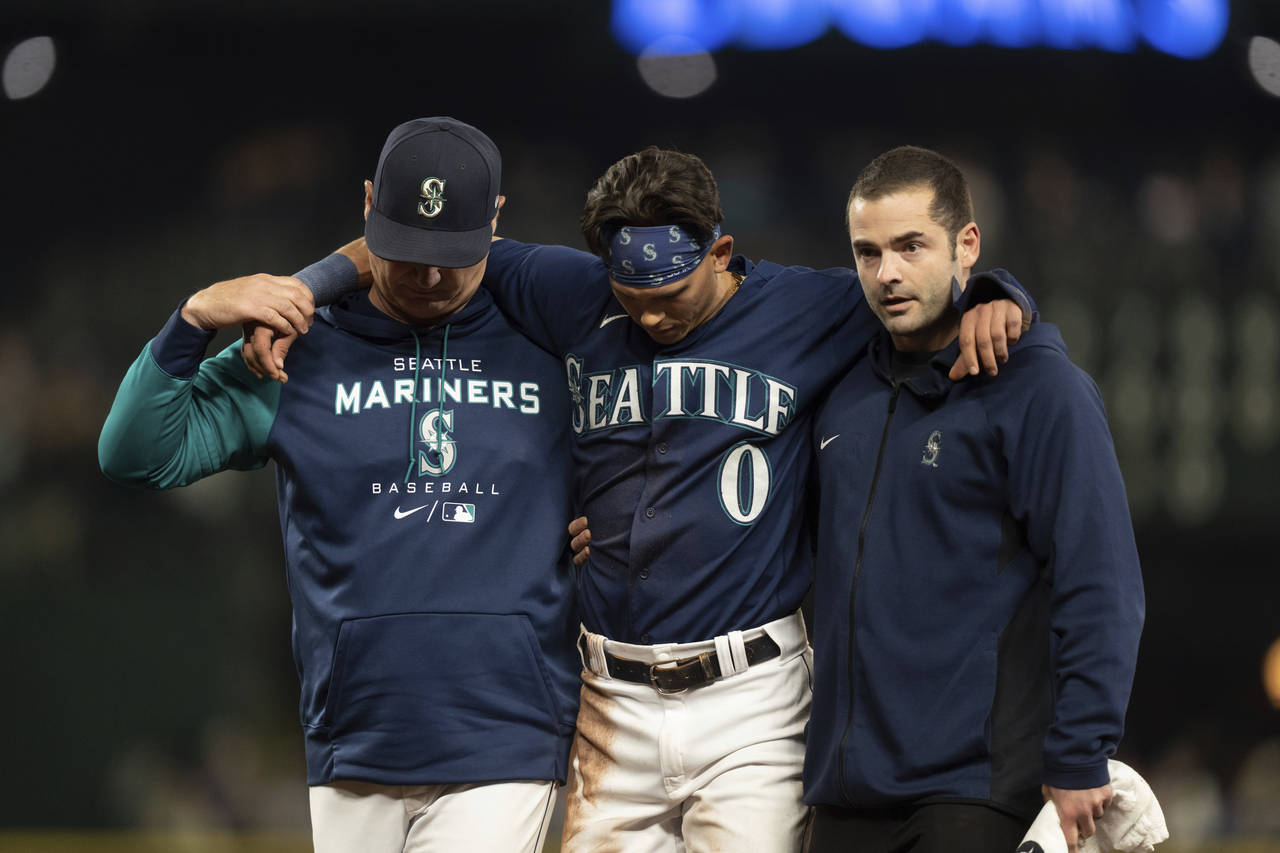 Seattle Mariners' Sam Haggerty, center, is helped off the field by training personnel manager Scott...