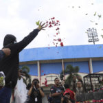 
              Supporters of local soccer club Arema FC throw flowers outside Kanjuruhan Stadium where riots broke out on Saturday night in Malang, East Java, Indonesia, Sunday, Oct. 2, 2022. Panic at the soccer match between Arema FC and Persebaya of Surabaya city left over 150 people dead, most of whom were trampled to death after police fired tear gas to dispel the riots. (AP Photo/Trisnadi)
            
