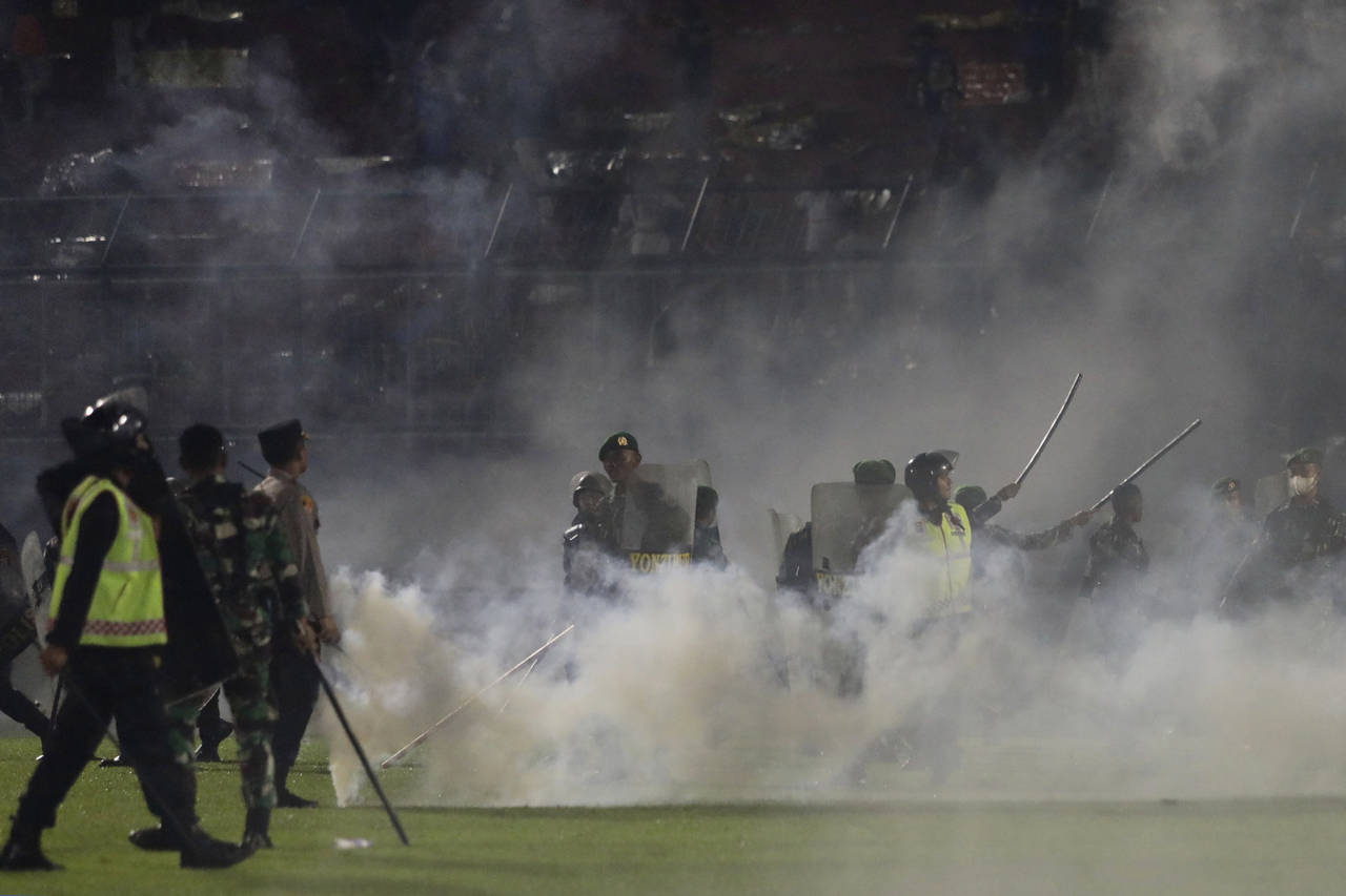 FILE - Police officers and soldiers stand amid tear gas smoke after clashes between fans during a s...