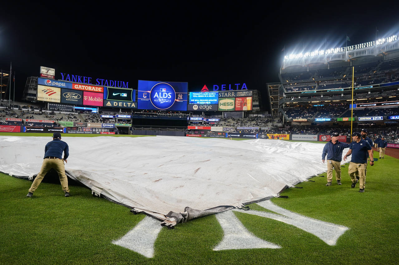 The Yankee Stadium grounds crew pulls the rain tarp over the field during a rain delay before Game ...