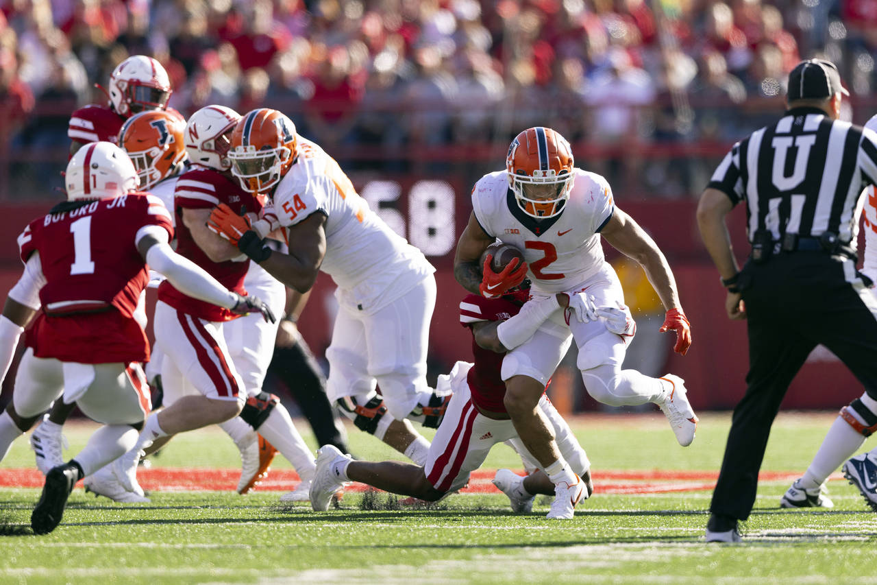 Illinois' Chase Brown (2) rushes as Nebraska's Myles Farmer (8) grabs him from behind during the fi...