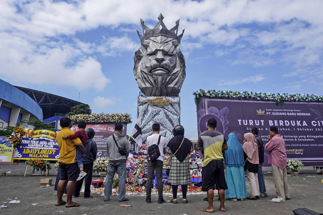 People offer prayers near the statue of a lion, the mascot of Arema FC, outside Kanjuruhan Stadium ...