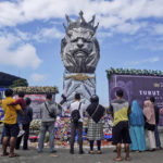 
              People offer prayers near the statue of a lion, the mascot of Arema FC, outside Kanjuruhan Stadium where a soccer stampede killed more than 100 people on Saturday, in Malang, East Java, Indonesia, Tuesday, Oct. 4, 2022. An Indonesian police chief and nine elite officers were removed from their posts Monday and 18 others were being investigated for responsibility in the firing of tear gas inside a soccer stadium that set off a stampede, officials said. (AP Photo/Dicky Bisinglasi)
            