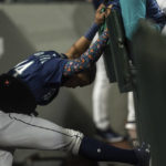 
              Seattle Mariners' Julio Rodriguez stretches in the dugout while wearing a device on his lower back during the fifth inning of a baseball game against the Detroit Tigers, Monday, Oct. 3, 2022, in Seattle. (AP Photo/Stephen Brashear)
            