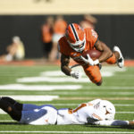 
              Oklahoma State running back Dominic Richardson (20) launches himself over Texas defensive back Anthony Cook, bottom, during the first half of an NCAA college football game Saturday, Oct. 22, 2022, in Stillwater, Okla. (AP Photo/Brody Schmidt)
            