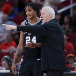
              San Antonio Spurs head coach Gregg Popovich, right, talks with Devin Vassell (24) by the bench during the first half of an NBA basketball game against the Houston Rockets Sunday, Oct. 2, 2022, in Houston. (AP Photo/Michael Wyke)
            