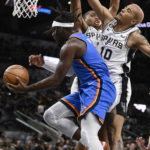 
              Oklahoma City Thunder's Luguentz Dort, left, goes to the basket while defended by San Antonio Spurs' Jeremy Sochan (10) and Keldon Johnson during the first half of a preseason NBA basketball game Thursday, Oct. 13, 2022, in San Antonio. (AP Photo/Darren Abate)
            