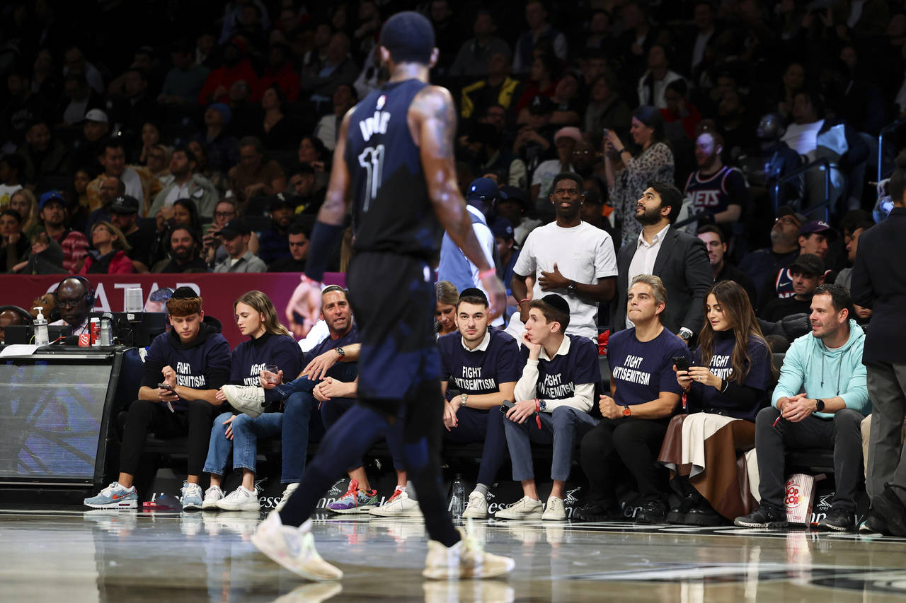 Fans with matching shirts look on as Brooklyn Nets guard Kyrie Irving (11) walks by during the firs...