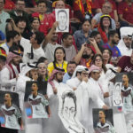 
              Spectators hold photos of Forman German international Mesut Ozil on the stands and cover their mouths during the World Cup group E soccer match between Spain and Germany, at the Al Bayt Stadium in Al Khor , Qatar, Sunday, Nov. 27, 2022. (AP Photo/Matthias Schrader)
            