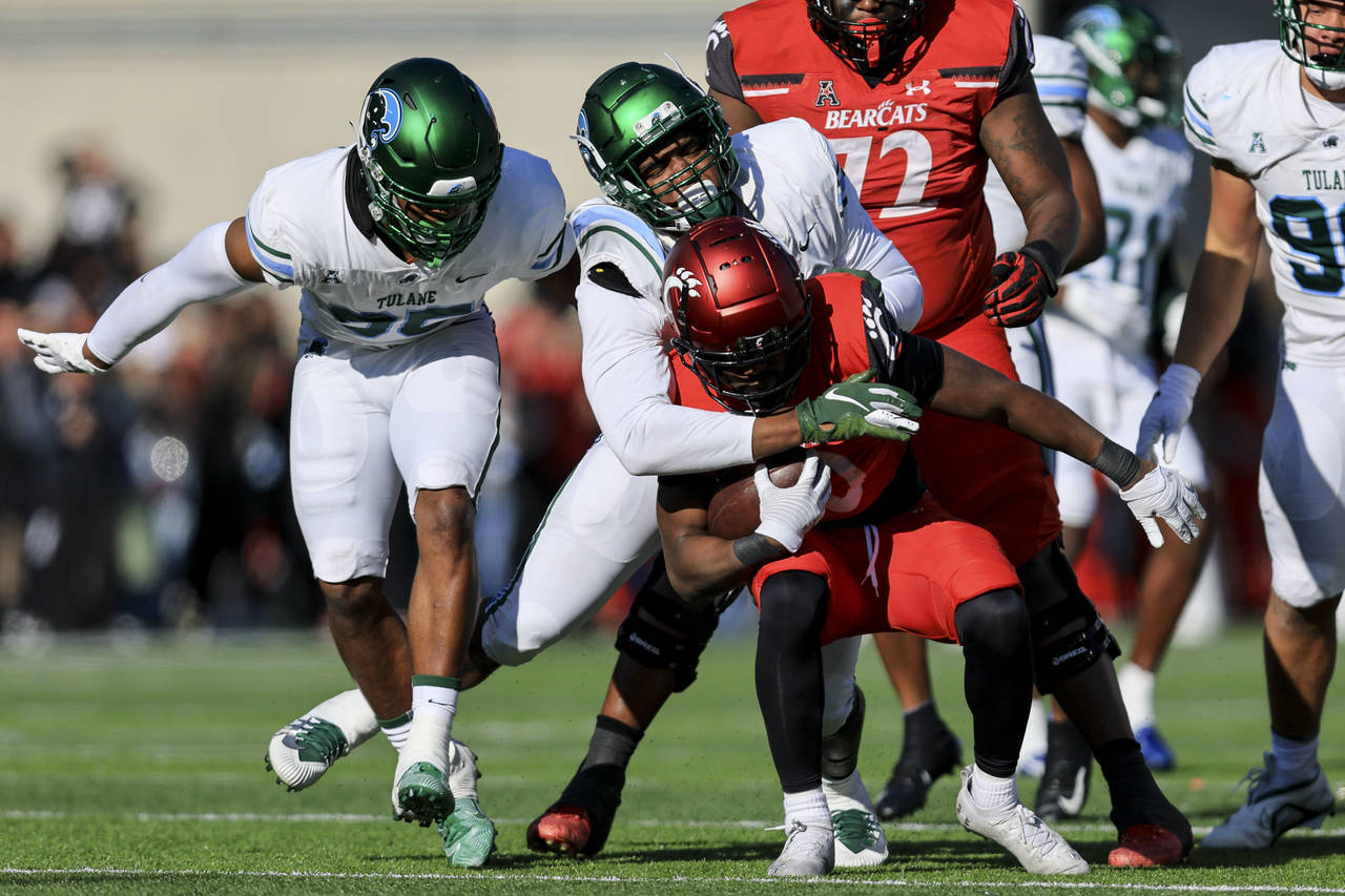 Cincinnati running back Charles McClelland, front, carries the ball as he is tackled by Tulane line...