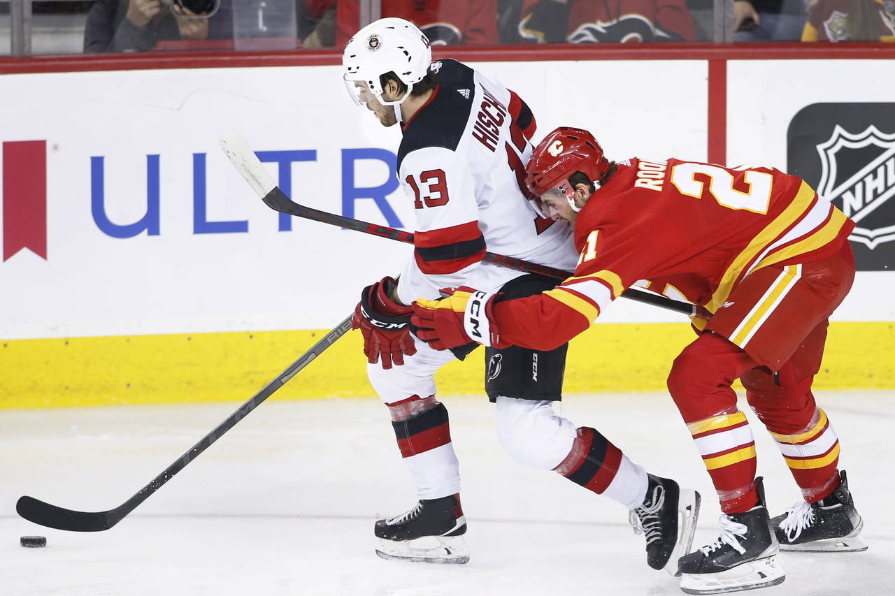 New Jersey Devils' Nico Hischier, left, reaches for the puck as Calgary Flames' Kevin Rooney defend...