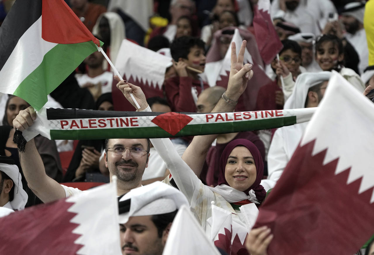 Fans wave the Palestinian flag and cheer prior the World Cup, group A soccer match between Qatar an...