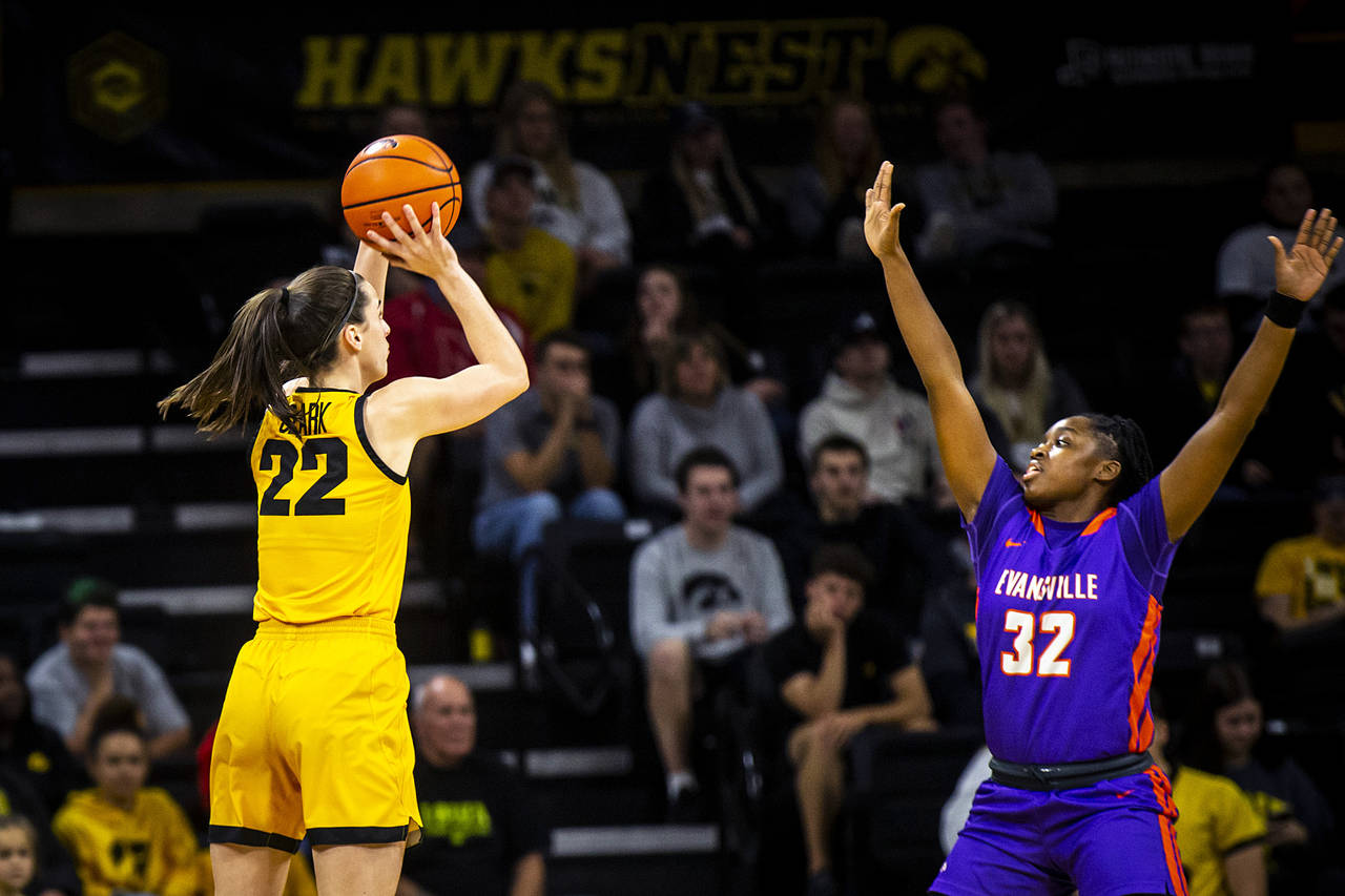 Iowa guard Caitlin Clark (22) shoots a 3-point basket as Evansville guard Myia Clark (32) defends d...