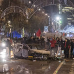 
              Moroccan soccer supporters cheer as they stand next to a burned out car in Brussels, Sunday, Nov. 27, 2022. Police had to seal off parts of the center of Brussels and moved in with water cannons and tear gas to disperse crowds following violence during and after Morocco's 2-0 win over Belgium at the World Cup. (AP Photo/Geert Vanden Wijngaert)
            