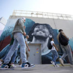 
              People walk past a mural of former Argentine player Diego Maradona, who led his country to the 1986 World Cup title, on a street prior to kick off the Qatar 2022 FIFA World Cup in Doha, Sunday, Nov. 20, 2022. (AP Photo/Eugene Hoshiko)
            