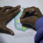 
              A student colors in a Brazilian football confederation crest, while waiting for the announcement of the list of players from the Brazil national team who will compete in the 2022 World Cup in Qatar, at the municipal school Paulo Reglus Neves Freire where the player Vinicius Jr. studied, in Sao Goncalo, Rio de Janeiro state, Brazil, Monday, Nov. 7, 2022. Four years ago teenager Vinicius Jr. took his first medal from a professional soccer tournament home, a place where drug gangs and vigilantes fight for control and children dribble past garbage on the streets. Today, Vinicius is a key figure on Brazil’s World Cup team. (AP Photo/Bruna Prado)
            