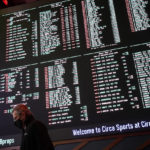 
              FILE - A man walks by as betting odds for NFL football's Super Bowl 55 are displayed on monitors at the Circa resort and casino sports book in Las Vegas, Feb. 3, 2021. Las Vegas oddsmakers had argued for years that sports betting is easier to monitor where it's legal and regulated. (AP Photo/John Locher, File)
            