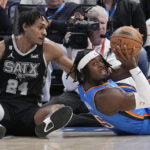 
              San Antonio Spurs guard Devin Vassell (24) reaches for the ball held by Oklahoma City Thunder forward Luguentz Dort, right, during the first half of an NBA basketball game Wednesday, Nov. 30, 2022, in Oklahoma City. (AP Photo/Sue Ogrocki)
            
