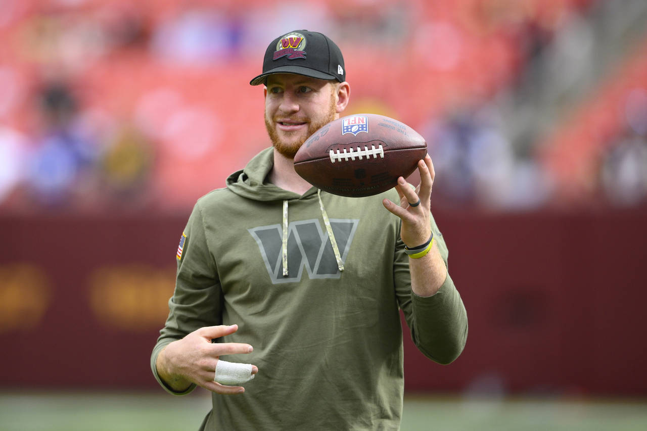 Injured Commanders quarterback Carson Wentz flips a football as he watches practice before the star...