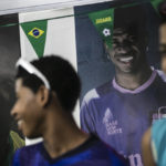 
              Photos of Vinicius Jr. cover the wall where students wait for coach Tite to announce his list of players for the 2022 soccer World Cup in Qatar, at the Paulo Freire municipal school where the player Vinicius Jr. studied, in Sao Goncalo, Rio de Janeiro state, Brazil, Monday, Nov. 7, 2022. Four years ago teenager Vinicius Jr. took his first medal from a professional soccer tournament home, a place where drug gangs and vigilantes fight for control and children dribble past garbage on the streets. Today, Vinicius is a key figure on Brazil’s World Cup team. (AP Photo/Bruna Prado)
            