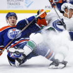 
              Vancouver Canucks defenseman Ethan Bear, right, is tripped by Edmonton Oilers forward Dylan Holloway during second-period NHL hockey game action in Edmonton, Alberta, Friday, Dec. 23, 2022. (Jeff McIntosh/The Canadian Press via AP)
            