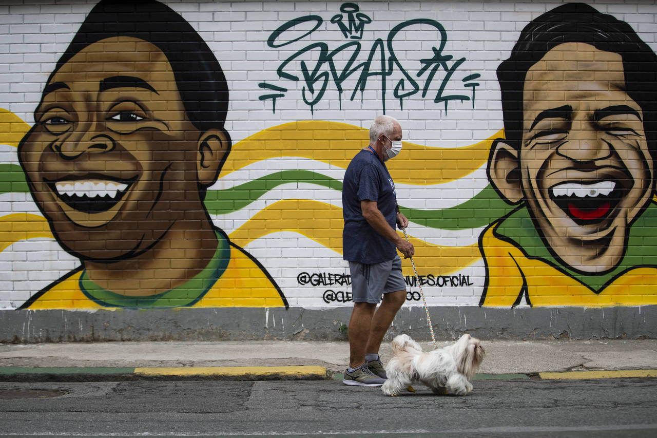 A man walks his dog past a mural of Brazilian soccer stars Pele, left, and Garrincha in Rio de Jane...