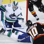 
              Vancouver Canucks defenseman Luke Schenn, right, attempts to block as shot from Calgary Flames forward Jonathan Huberdeau, center, as goalie Spencer Martin stops it during the first period of an NHL hockey game in Calgary, Alberta on Wednesday, Dec. 14, 2022. (Jeff McIntosh/The Canadian Press via AP)
            