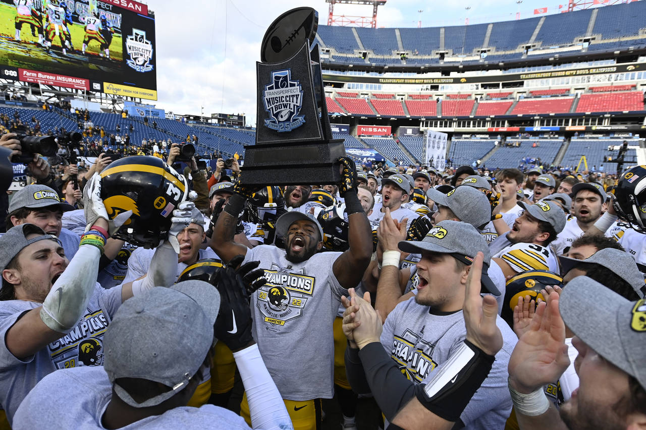 Iowa defensive back Dallas Craddieth, center, holds up the trophy as he celebrates with teammates a...