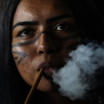 
              A Pataxo Indigenous woman smokes a traditional pipe during the Meeting of the First Peoples' ceremony at the 18th annual Free Land Indigenous Camp in Brasilia, Brazil, on April 8, 2022. (AP Photo/Eraldo Peres)
            