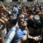 
              Soccer fans look up for water thrown by residents in Buenos Aires, Argentina Tuesday, Dec. 20, 2022. Fans descended into the streets of the capital eager to catch a glimpse of the open-top bus carrying the Argentine national soccer team that won the World Cup final. (AP Photo/Mario De Fina)
            