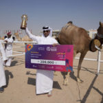 
              Fayez Ahmed alKuwari poses with the trophy and a money prize after winning with his family of camel owners the first prize at a camel pageant at the Qatar camel Mzayen Club, in Ash- Shahaniyah, Qatar, Friday, Dec. 2, 2022. (AP Photo/Alessandra Tarantino)
            