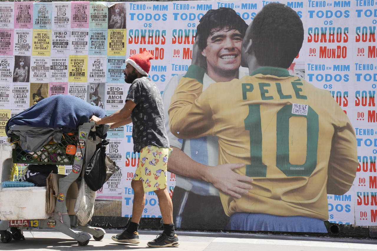 A man pushes a cart loaded with garbage for recycling in front of a mural depicting Brazilian socce...
