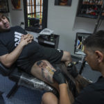 
              Artist César "Yeyo" Molina tattoos Sebastian Fernandez's leg, featuring a large image of soccer player Lionel Messi with the World Cup trophy, in Buenos Aires, Argentina, Thursday, Dec. 29, 2022. (AP Photo/Victor R. Caivano)
            
