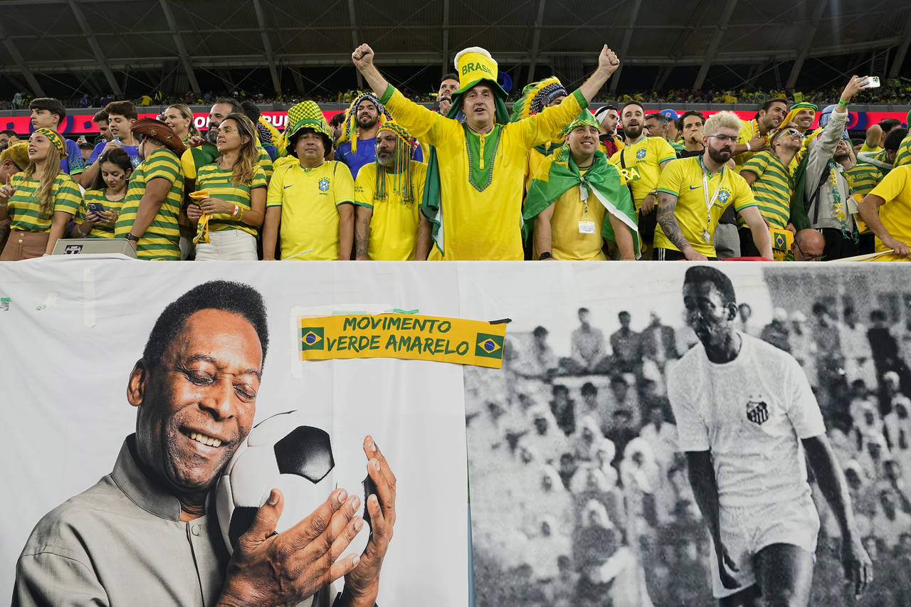 Brazil supporters cheer on the stands above a banner with pictures of soccer legend Pele, while wai...