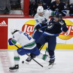 
              Vancouver Canucks' Conor Garland (8) picks up the puck as teammate Curtis Lazar (20) takes Winnipeg Jets' Karson Kuhlman (20) out of the play during second-period NHL hockey game action in Winnipeg, Manitoba, Thursday, Dec. 29, 2022. (John Woods/The Canadian Press via AP)
            