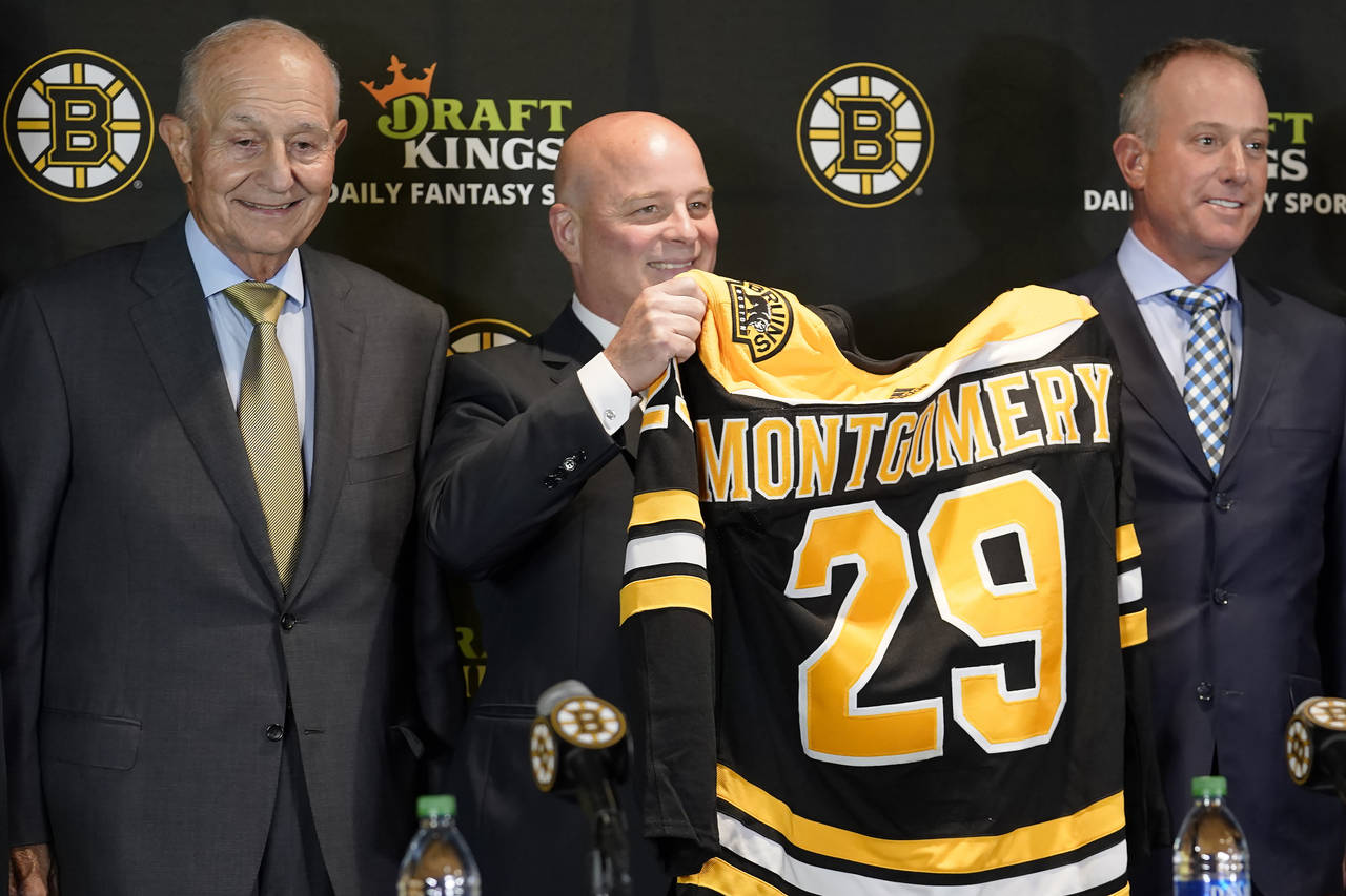 Boston Bruins newly hired head coach Jim Montgomery, center, displays a Bruins jersey while standin...