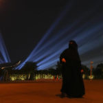 
              A woman wearing traditional clothing walks as a drone display shows the likeness of the World Cup soccer trophy in Doha, Qatar, Friday, Dec. 2, 2022. (AP Photo/Julio Cortez)
            