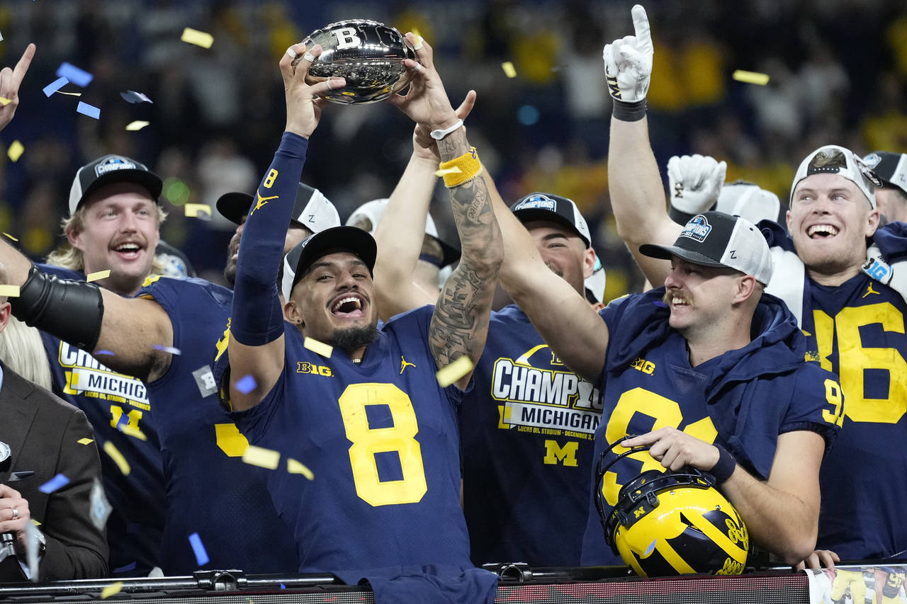 Michigan wide receiver Ronnie Bell holds the trophy as he celebrates with teammates after defeating...