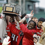
              Louisville head coach Deion Branch holds up the trophy as his players celebrate around him after their 24-7 win over Cincinnati in the Fenway Bowl NCAA college football game at Fenway Park Saturday, Dec. 17, 2022, in Boston. (AP Photo/Winslow Townson)
            