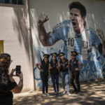 
              Students graduating from the General Las Heras elementary school, where Lionel Messi also attended school, pose for a group photo wearing their graduation hats by a mural of Messi, on the last day of school in Rosario, Argentina, Wednesday, Dec. 14, 2022. (AP Photo/Rodrigo Abd)
            