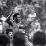 
              FILE - Soccer superstar Pele, waving the flags of Brazil and the U.S., is carried off the field in driving rain by players of both teams at Giants Stadium in East Rutherford, N.J., after his final game, Oct. 1, 1977. Pelé, the Brazilian king of soccer who won a record three World Cups and became one of the most commanding sports figures of the last century, died in Sao Paulo on Thursday, Dec. 29, 2022. He was 82. (AP Photo/Richard Drew, File)
            
