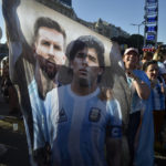 
              A flag featuring Lionel Messi, left, and the late soccer great Maradona hangs amid Argentina soccer fans after they watched the team's World Cup semifinal win over Croatia, hosted by Qatar, on a screen set up in the Palermo neighborhood of Buenos Aires, Argentina, Tuesday, Dec. 13, 2022. (AP Photo/Gustavo Garello)
            